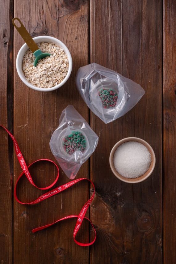 Overhead view of piping bags inside cups, being filled with reindeer food ingredients, surrounded by small bowls of oats and sugar.