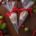 Overhead view of two piping bags filled with reindeer food tied with red bows, surrounded by scattered Christmas ornaments on a wooden tabletop.