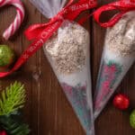 Overhead view of two piping bags filled with reindeer food tied with red bows, next to Christmas ornaments on a wooden tabletop.