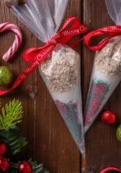 Overhead view of two piping bags filled with reindeer food tied with red bows, next to Christmas ornaments on a wooden tabletop.