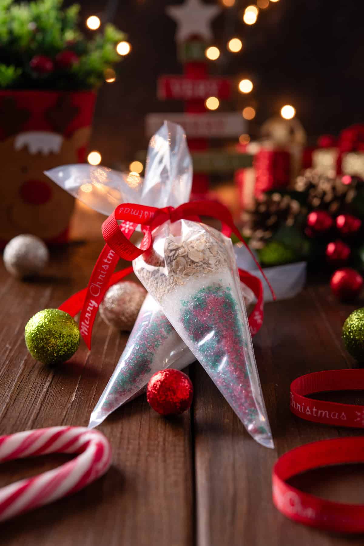 Two piping bags filled with reindeer food tied with red bows, next to candy canes and scattered Christmas lights and ornaments on a wooden tabletop.