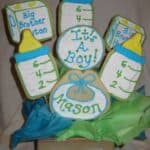 Seven Baby-Themed Sugar Cookies Sticking Out of a Square Bowl with a Bow on It