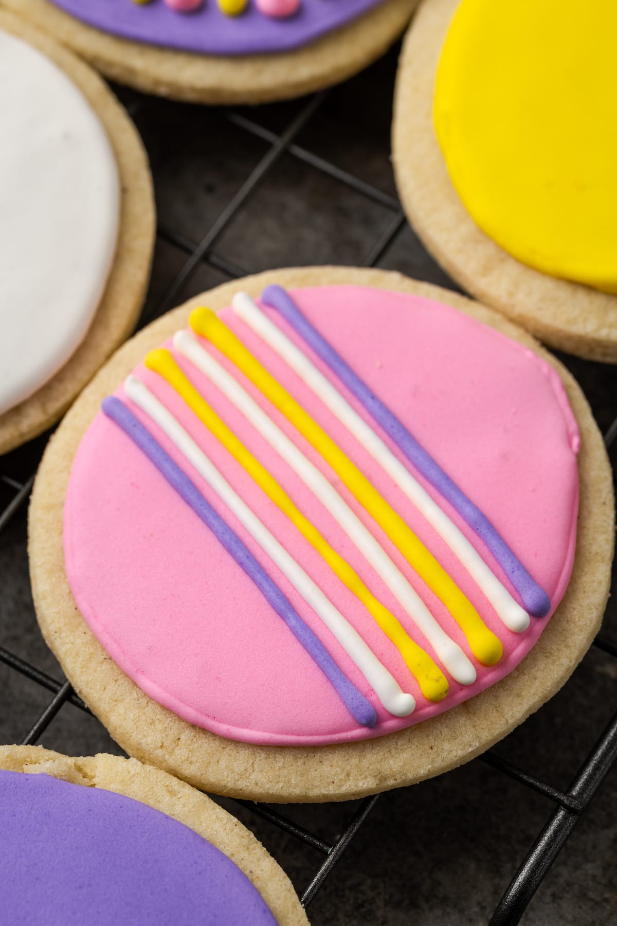 Close up of a round sugar cookie decorated with stripes of royal icing, next to more decorated cookies.