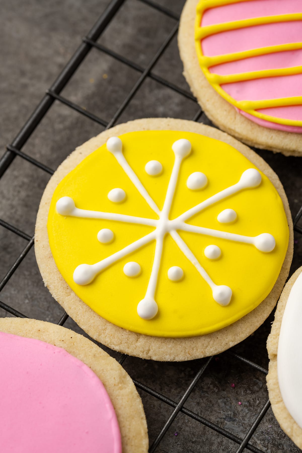 Close up of a round sugar cookie decorated with royal icing in a snowflake design, next to more decorated cookies.
