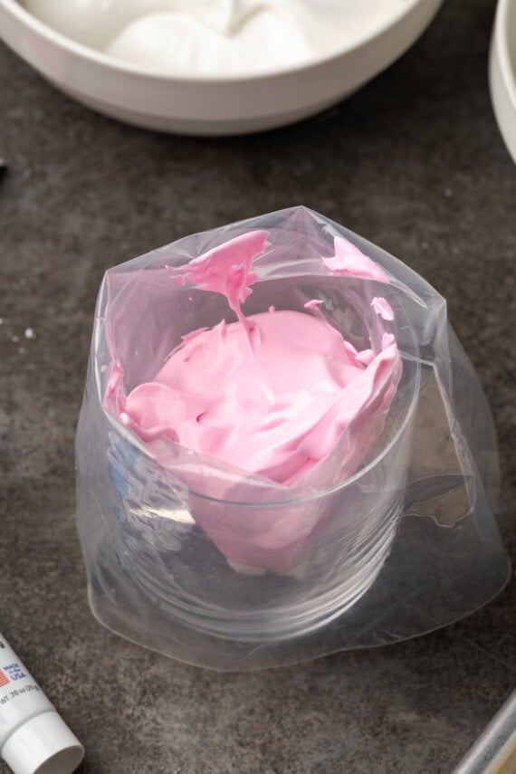 Pink royal icing added to an open piping bag resting in a glass.