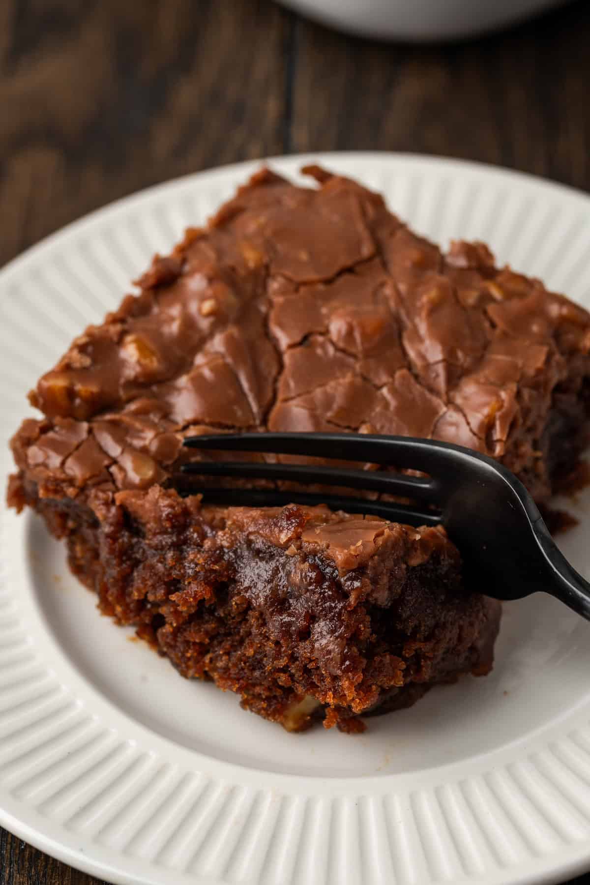 A fork cuts into the corner of a slice of Coca Cola cake on a white plate.