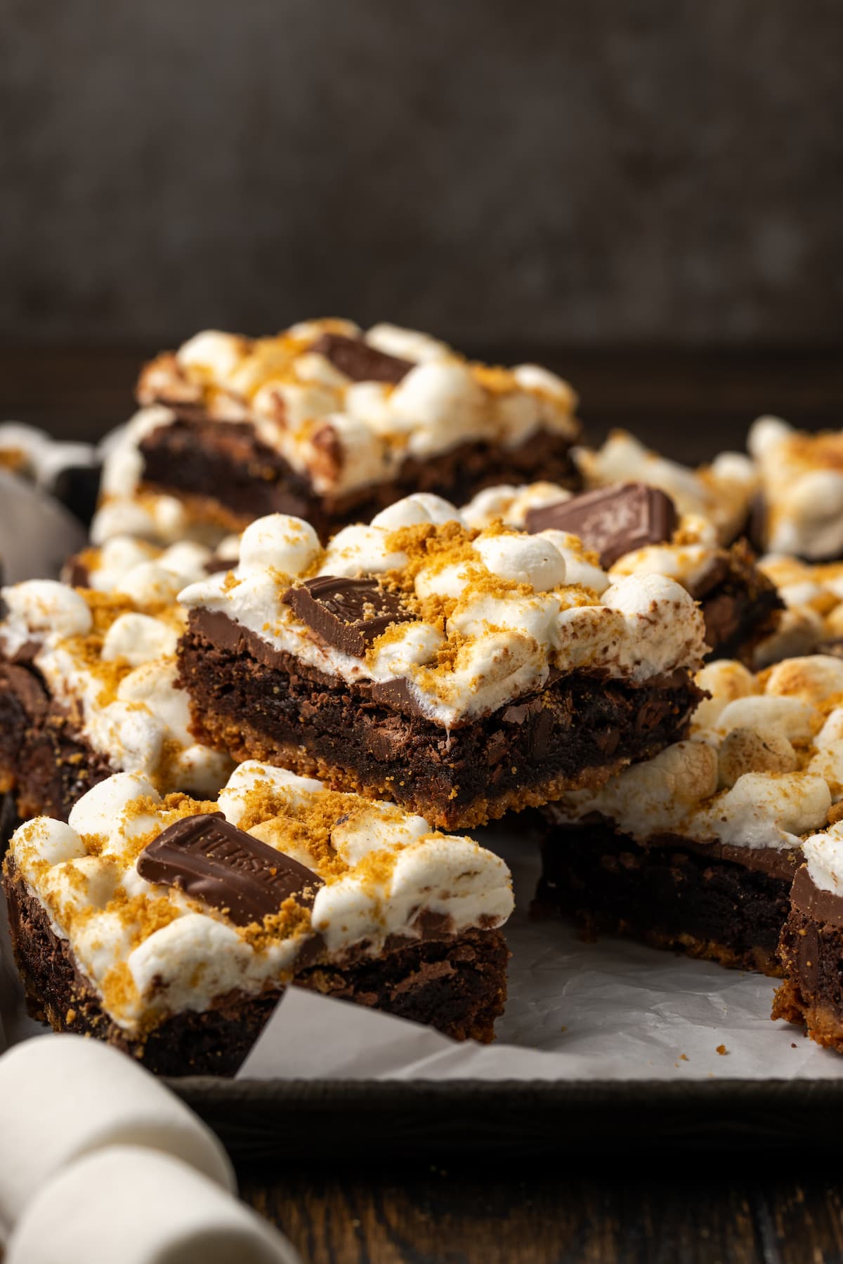 Assorted smores brownies stacked on a parchment-lined board.