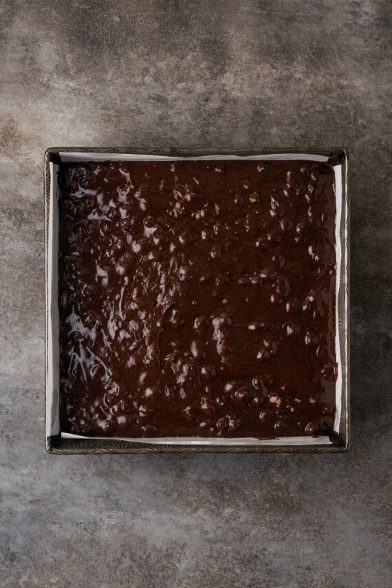 Brownie batter in a lined square baking pan.