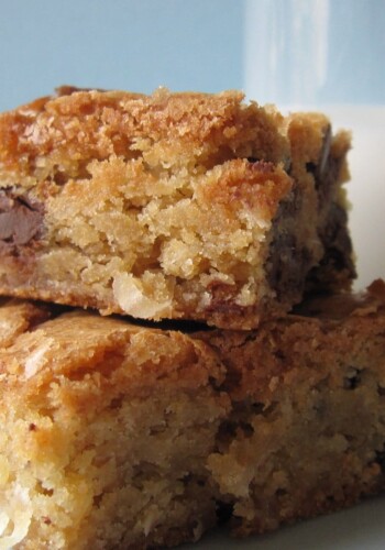 A close-up of two chocolate chip blondies stacked next to a glass of milk