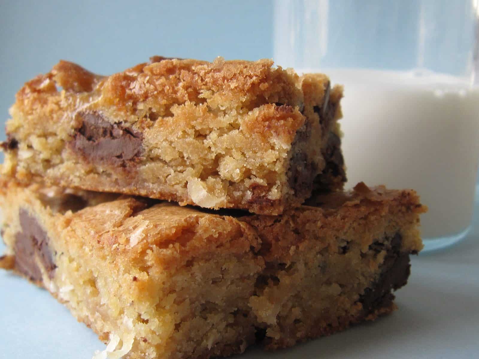 A close-up of two chocolate chip blondies stacked next to a glass of milk