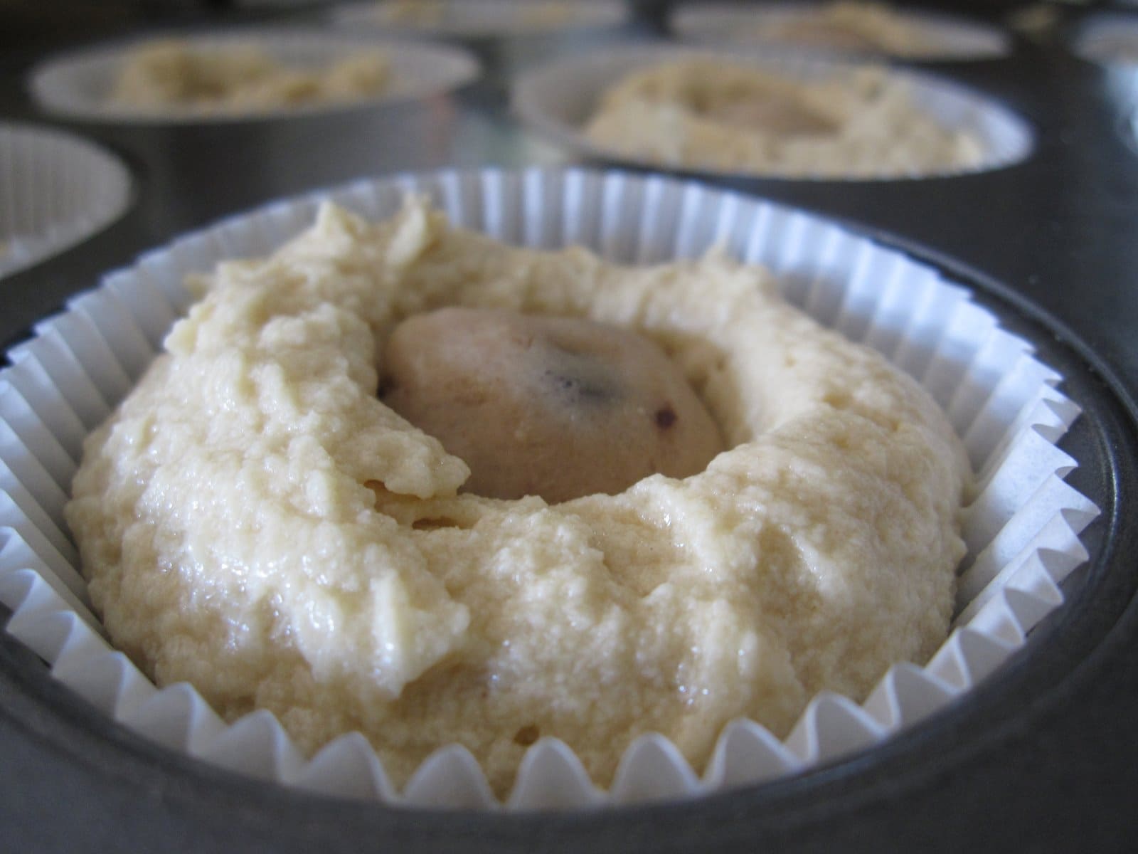 Close-up of a muffin cup with cupcake batter and a piece of frozen cookie dough