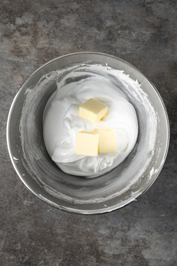 Cubed butter added to whipped meringue in a bowl.