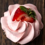 Overhead close up view of a frosted strawberry cupcake topped with a fresh strawberry half.