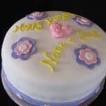 Carrot Cake Decorated with White Fondant, Pink and Purple Flowers, and Yellow Happy Birthday Icing