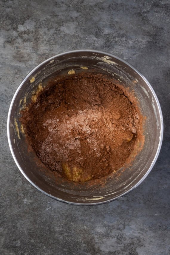 Dry ingredients added to chocolate cake batter in a metal mixing bowl.