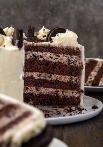 A decorated four-layer cookies and cream cake with a large slice cut out, revealing the cake layers filled with Oreo frosting.
