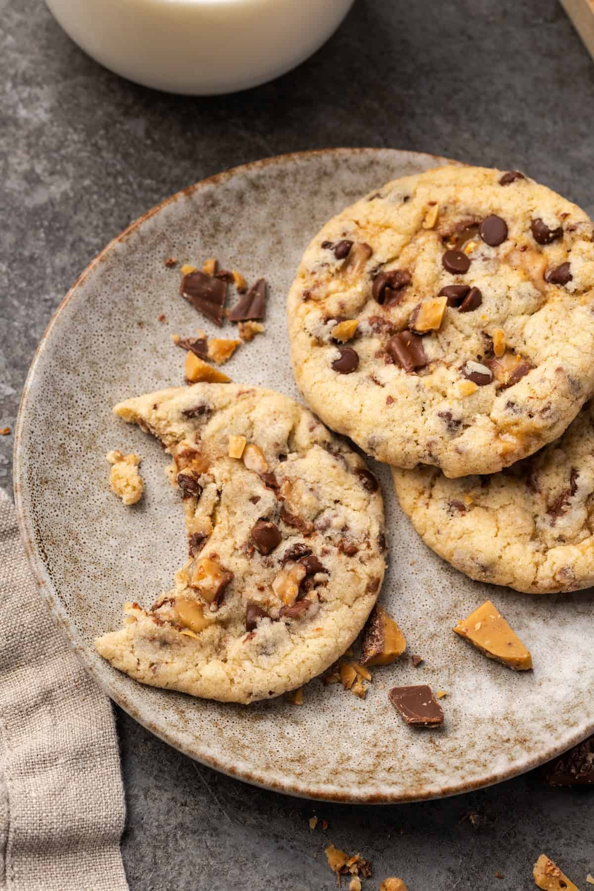 Overhead view of toffee chocolate chip cookies on a stoneware plate with a bite missing from one cookie.