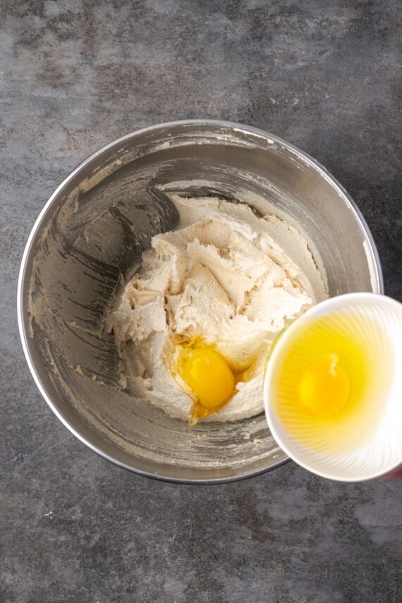 Adding eggs to cookie dough ingredients in a metal bowl.