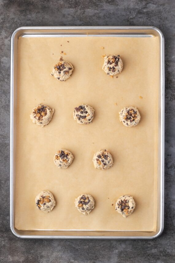 Toffee chocolate chip cookie dough balls on a parchment-lined baking sheet.