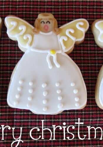 Three Angel Sugar Cookies Lined Up Over a Plaid Tablecloth