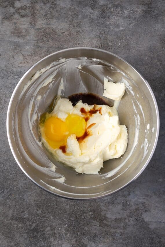 Egg and vanilla added to the cheesecake batter in a mixing bowl.