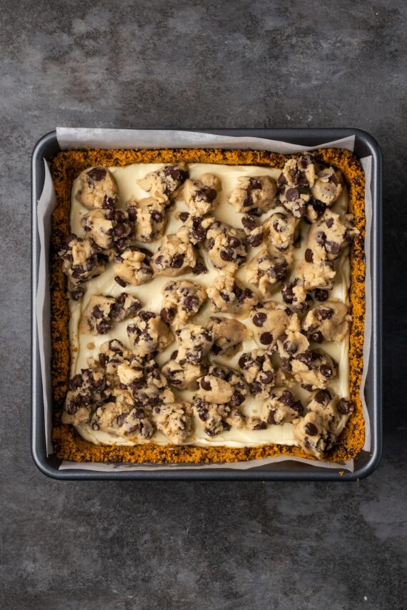 Balls of cookie dough added on top of the cheesecake bars in a baking pan.