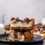 Side view of two chocolate chip cheesecake bars stacked on a black stoneware plate.