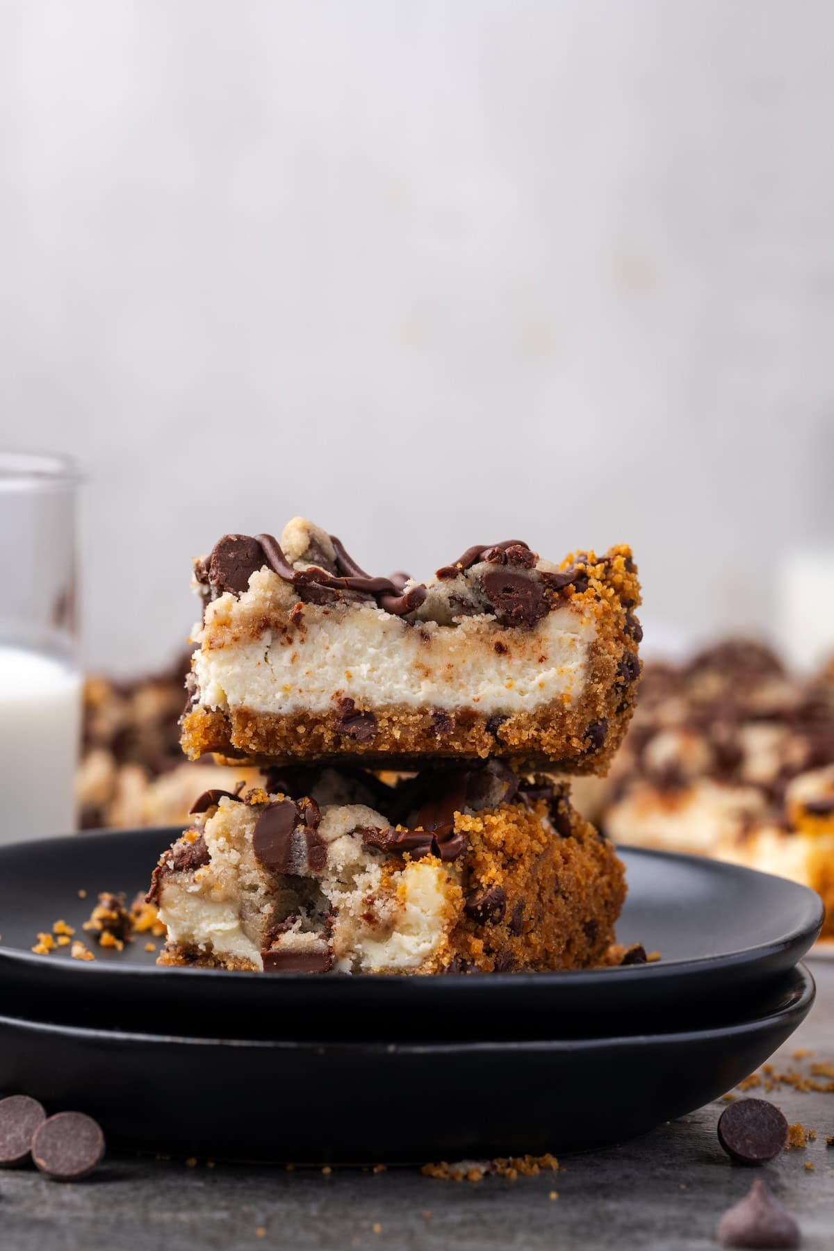 Side view of two chocolate chip cheesecake bars stacked on a black stoneware plate.