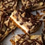 Assorted chocolate chip cheesecake bars on a sheet of parchment paper, with one bar propped up against the bars around it.
