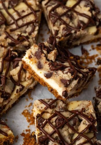 Assorted chocolate chip cheesecake bars on a sheet of parchment paper, with one bar propped up against the bars around it.