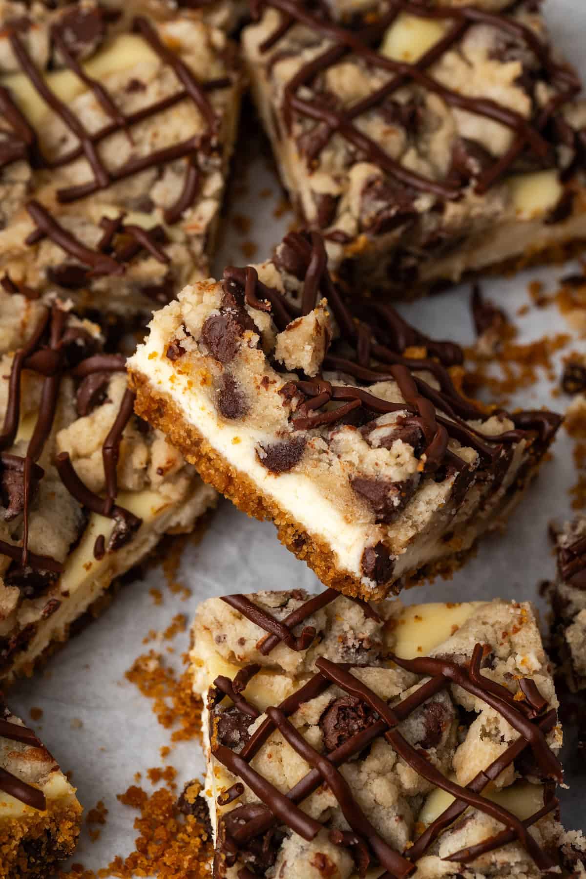 Assorted chocolate chip cheesecake bars on a sheet of parchment paper, with one bar propped up against the bars around it.