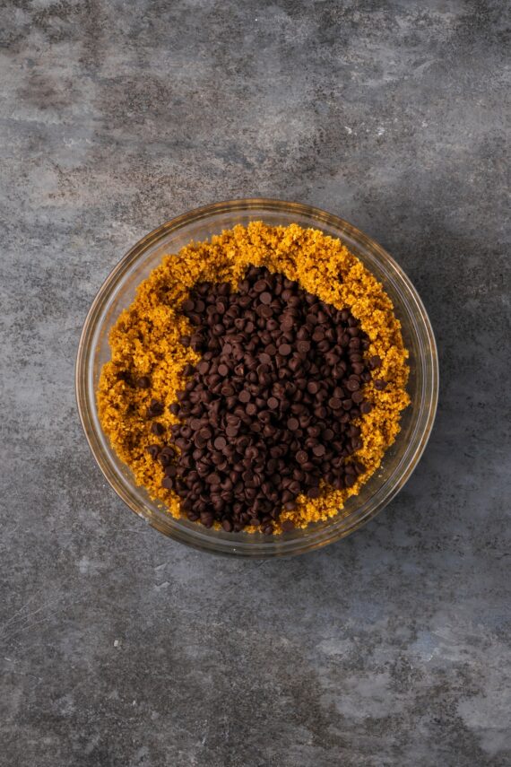 Chocolate chips added to the graham cracker crust mixture in a bowl.
