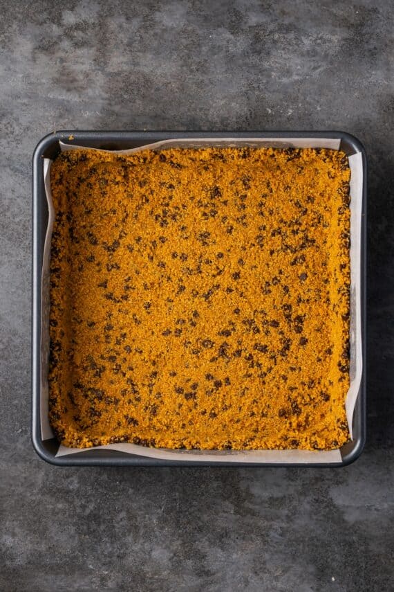 Chocolate chip graham cracker crust pressed into the bottom of a lined square baking pan.