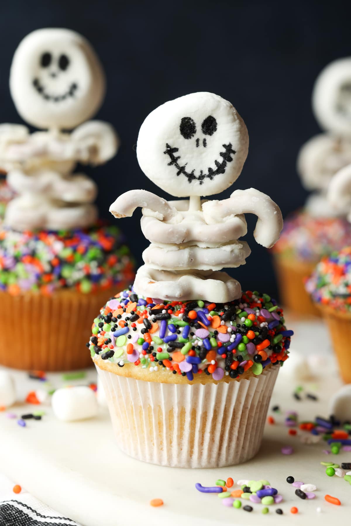 A halloween cupcake topped with a skeleton made from marshmallows and white chocolate covered pretzels