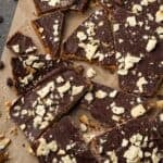 Assorted saltine toffee pieces scattered on a sheet of parchment paper.
