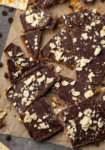 Assorted saltine toffee pieces scattered on a sheet of parchment paper.