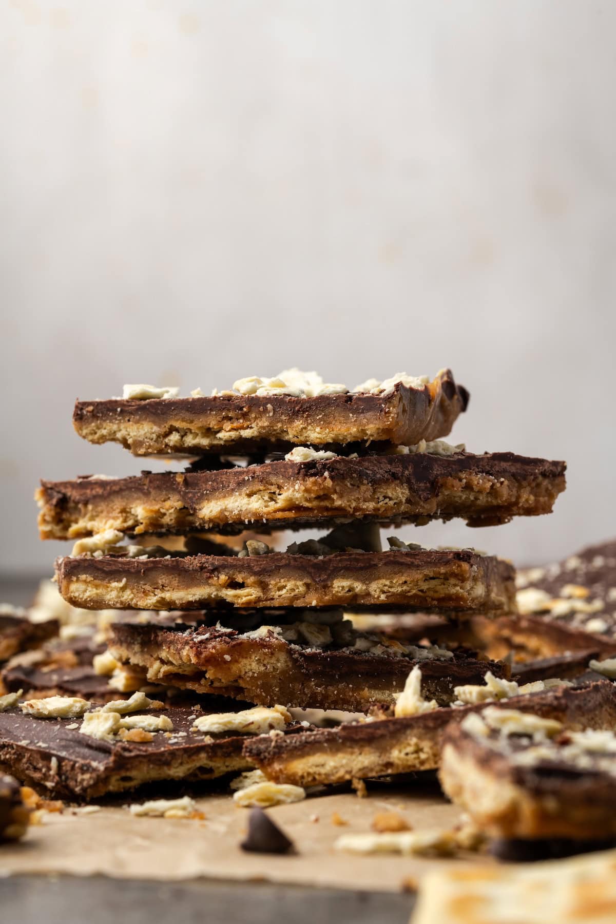 Side view of saltine toffee stacked on a sheet of parchment, surrounded by more toffee pieces.