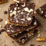 Saltine toffee stacked on a sheet of parchment, surrounded by more toffee pieces.