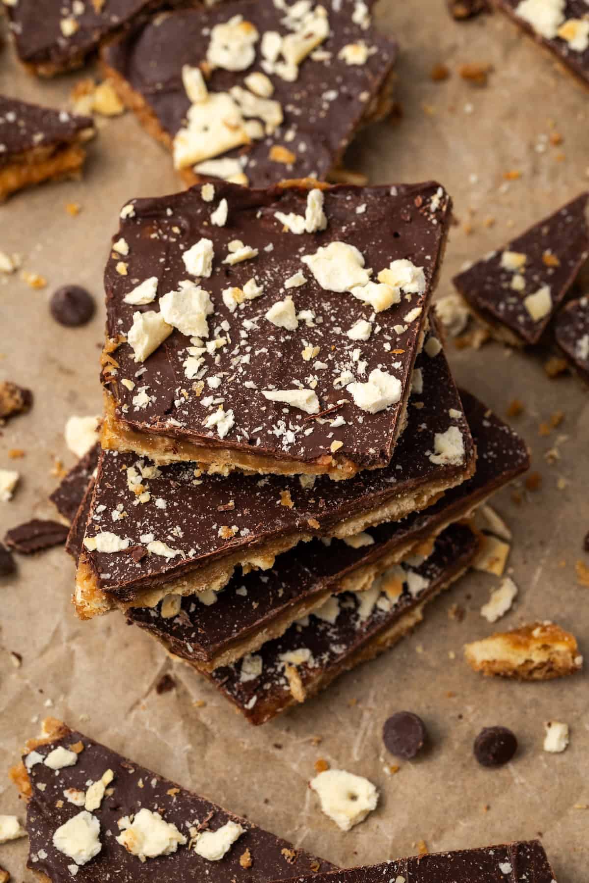 Saltine toffee stacked on a sheet of parchment, surrounded by more toffee pieces.