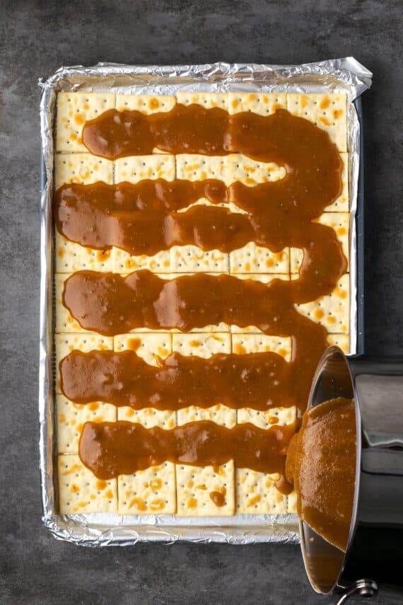 Pouring melted toffee over saltine crackers on a baking sheet.