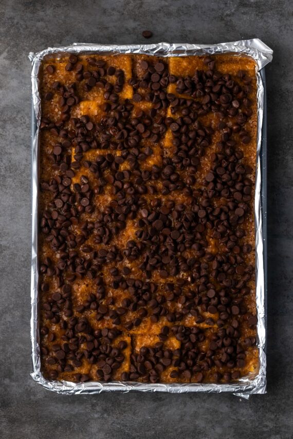 Warm saltine toffee covered with chocolate chips on a baking sheet.