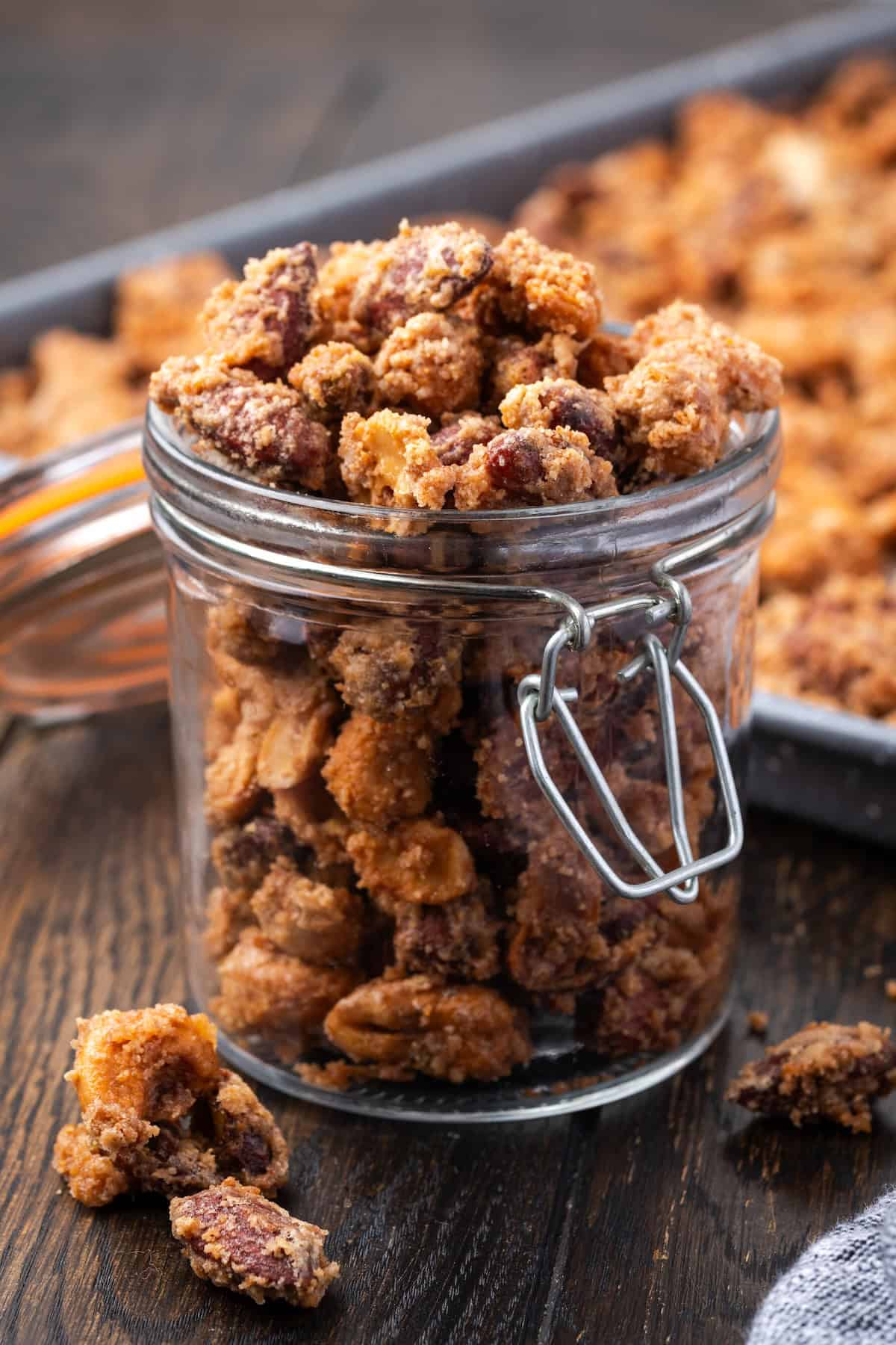 Mashuga nuts in a glass jar with a lid with more nuts on a baking sheet in the background.