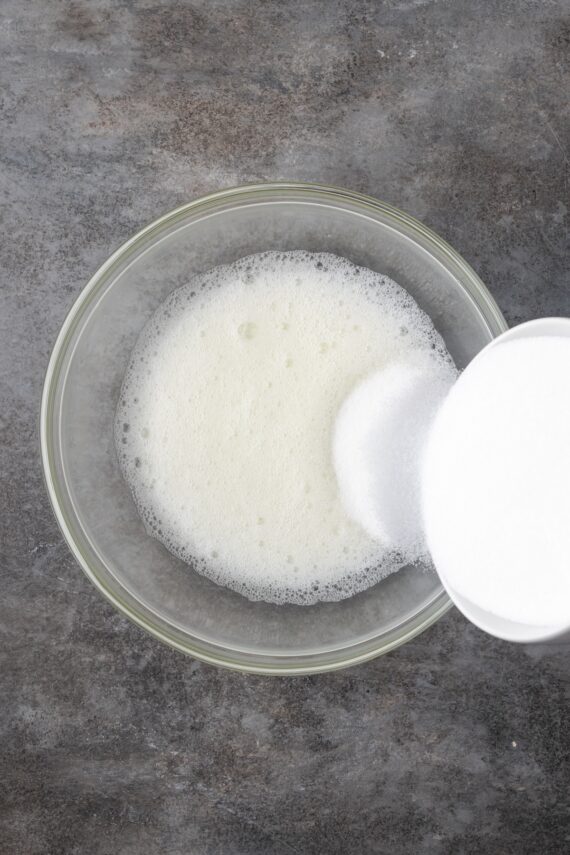 Adding sugar to a bowl of whipped meringue.