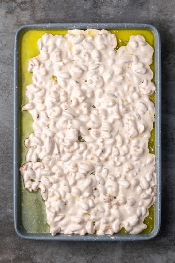 Mixed nuts covered with meringue spread out on a baking sheet.