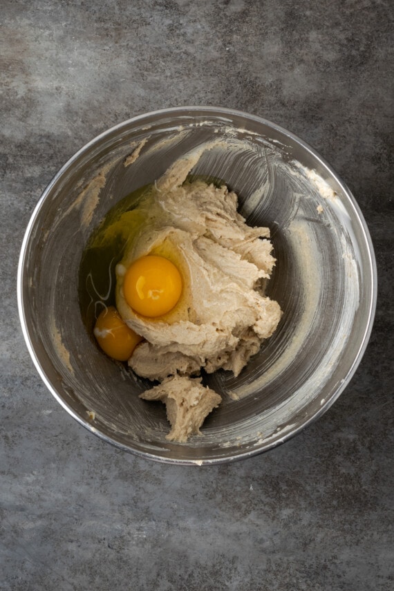 Eggs added to a metal mixing bowl with creamed butter and sugar.