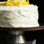 Side view of a lemonade cake on a cake stand with lemon peel on top