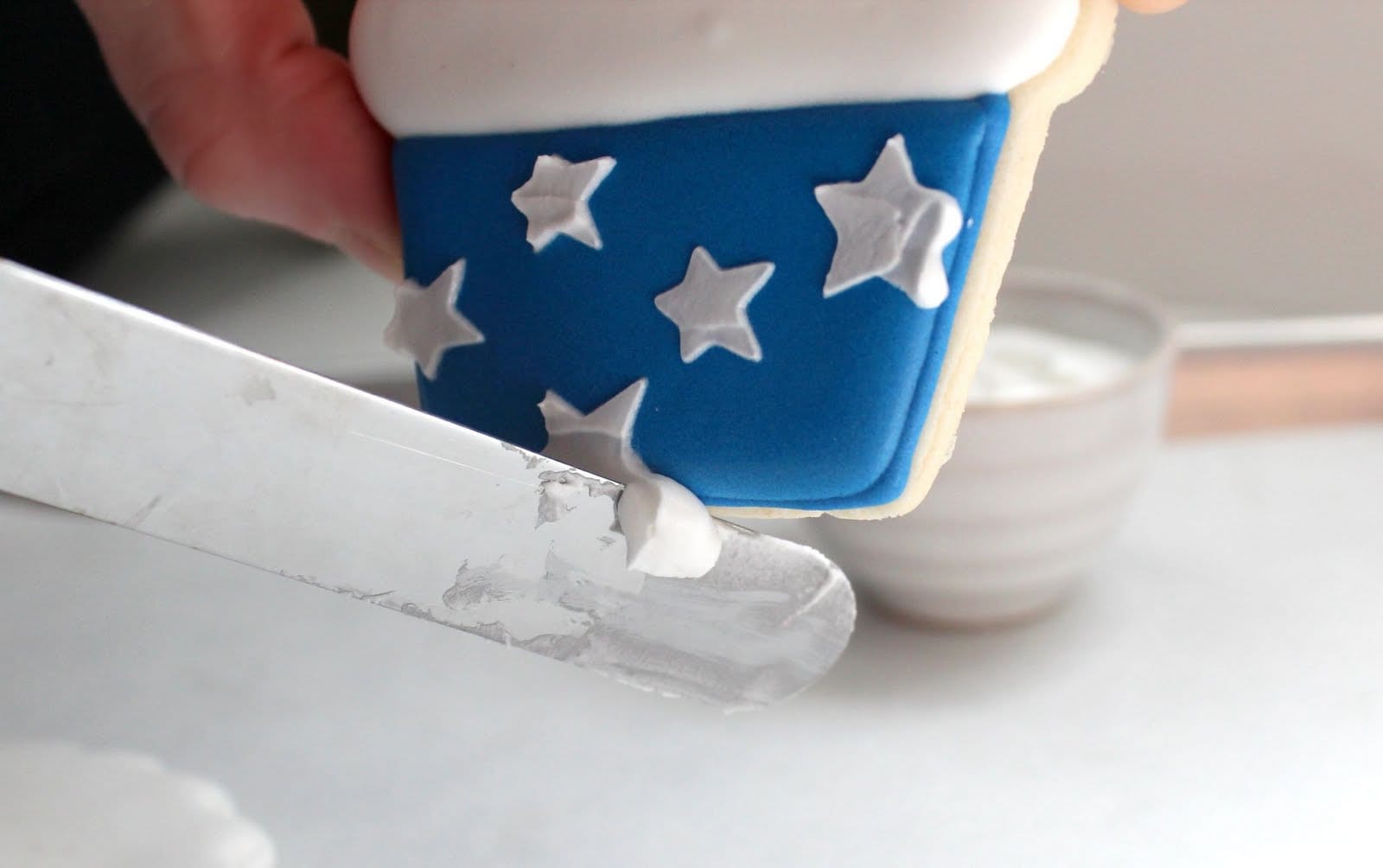 A knife removing extra frosting from a cupcake-shaped cookie