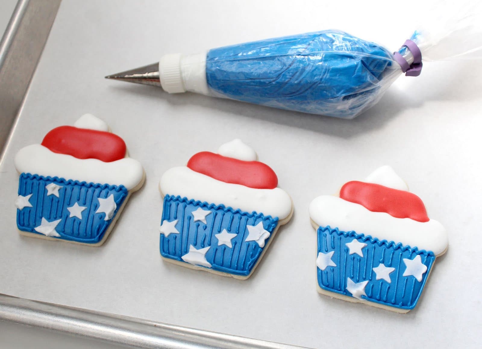 Blue frosting in a piping bag with 3 stars and stripes cupcake cookies 