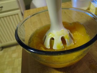 A hand blender combines the ingredients for peach wine cupcakes in a mixing bowl.