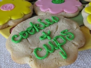 An eggless sugar cookie with "Cookies and Cups" spelled out in green icing.